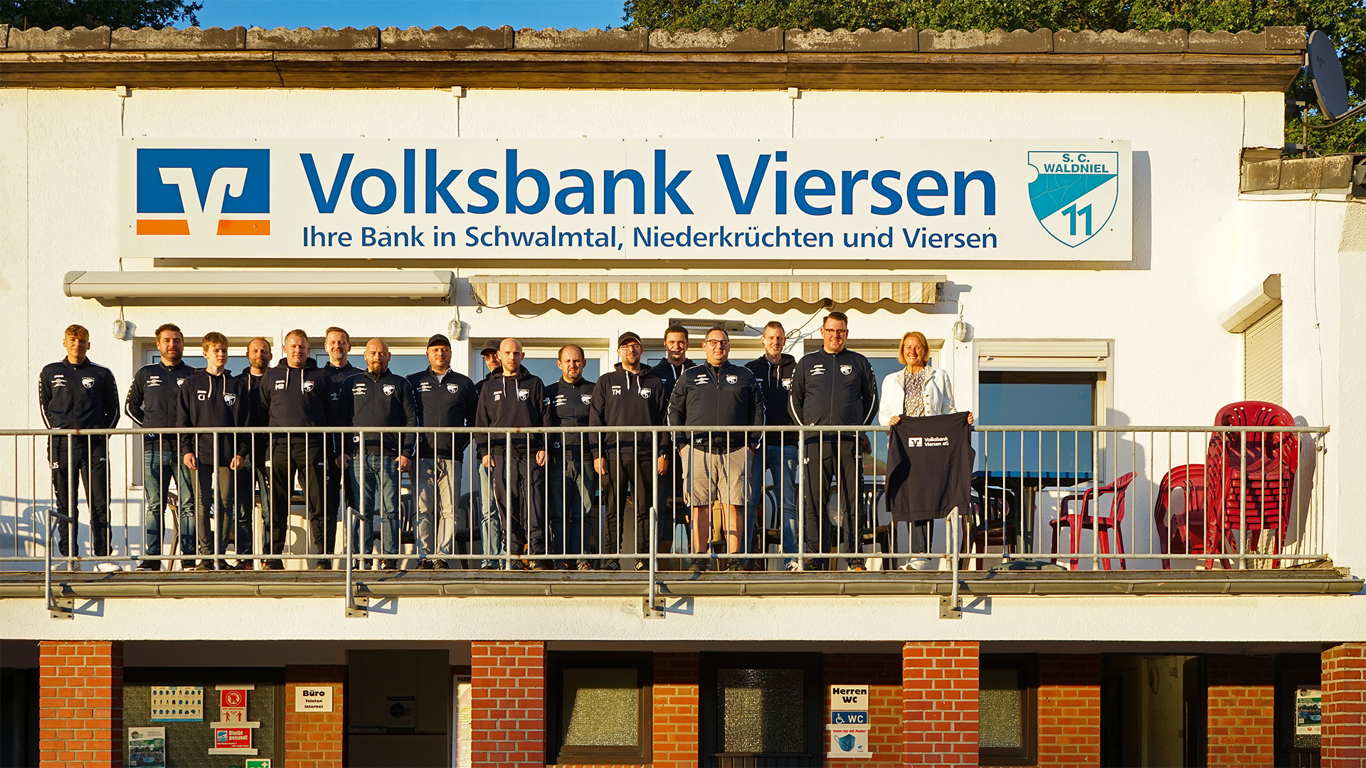 Gruppenbild mit Dame: Stephanie Krähenhöfer, Leiterin der Waldnieler Geschäftsstelle der Volksbank Viersen, und ein Teil des Trainerstabs des SC Waldniel präsentieren die neue Ausstattung.